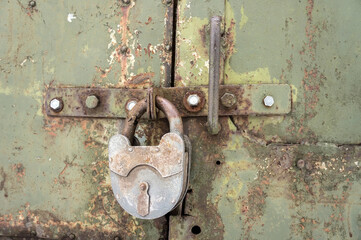 An old rusty padlock on a rusty metal door