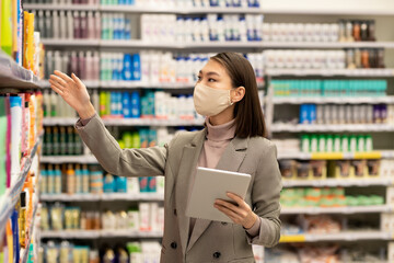 Young Asian female consumer with tablet choosing bodycare products for herself
