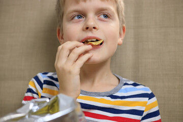 Little boy sitting on sofa, eating chips from packet