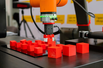 Pick and place robotic clamp arm manipulator moving red toy blocks at modern robot exhibition, trade show - close up view. Manufacturing, industrial, engineering, ai, automated technology concept