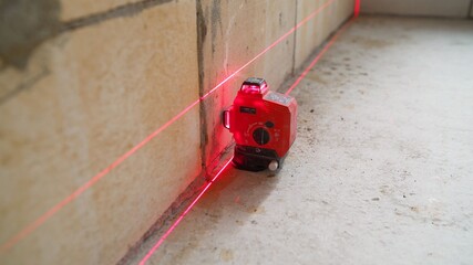 The construction laser level is on the floor. The beam is directed at the wall. Aligning the walls with a laser level.