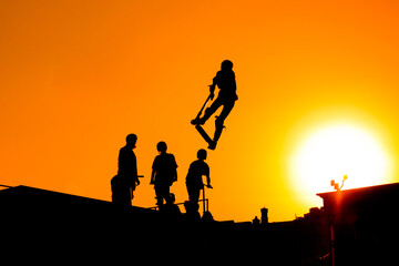 Fototapeta na wymiar Unrecognizable teenage boy silhouette showing high jump tricks on scooter against orange sunset sky at skatepark. Sport, freestyle, extreme, youth, urban culture, outdoor activity concept