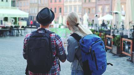 Back view of young man and woman with bags checking map on central city square. They discussing their new destination.