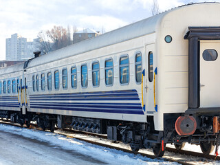 The white railroad car of the train stands on the tracks on a bright winter day.