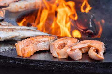 Process of grilling salmon steaks and mackerel fish on black brazier at summer local food market - close up. Outdoor cooking, barbecue, gastronomy, seafood, cookery, street food concept
