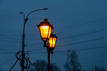 A vintage lamppost with burning lamps, blue sky at dusk