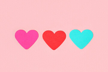 Three multi-colored hearts cut from paper on a pink background. Different love of all colors.