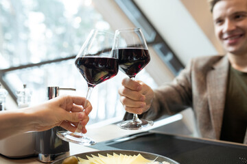 Hands of happy guy and those of his girlfriend clinking by glasses of red wine