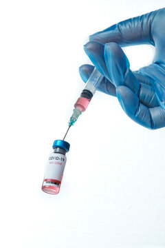 Nurse's hand with blue gloves loading covid-19 vaccine into a syringe.