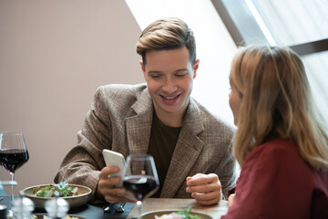 Happy young man looking at screen of smartphone while watching curious video