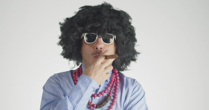 Front view of a curly-haired man wearing white eyeglasses smoking the cigar  and looking at the camera with a menacing gaze  isolated on gray background. 