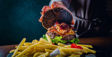 Chefs woman hand open burger with beaf steak vegetables and french fries