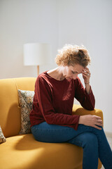 Woman with knee and headache problem sitting on a couch at home.