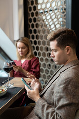 Young serious man and woman in smart casualwear scrolling in their smartphones