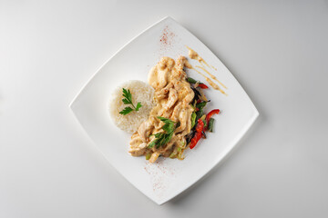 Slices of chicken breast fillet in cream sauce with rice and vegetables, top view