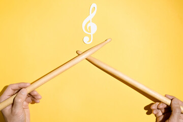 Drummer concept. Male hands holding drumsticks and a paper treble clef and musical treble clef. Flat lay