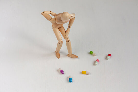 a bent wooden mannequin with back pain among colorful pills on white background
