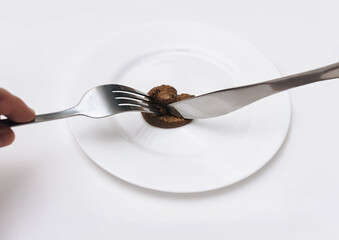 The client holds a fork and knife and cuts artificial plastic feces. Expired product. The concept of an inept cook, fake news, a crappy restaurant, bad food, a taste of shit. Bad smelling joke.