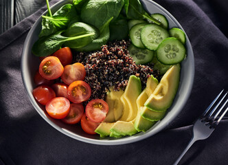 Top view on a bowl with tomato, cucumber, basil, avocado and quinoa