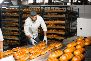 A baker collects hot bread that leaves an industrial oven in a bakery. Industrial bread production