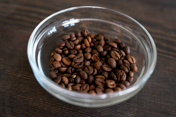 Glass bowl with roasted coffee beans on wooden table prepared for grinding