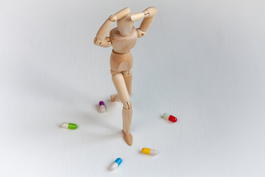a wooden mannequin with headache among colorful pills on white background