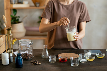 Young woman holding glassware with melted soap mass over table with glassware