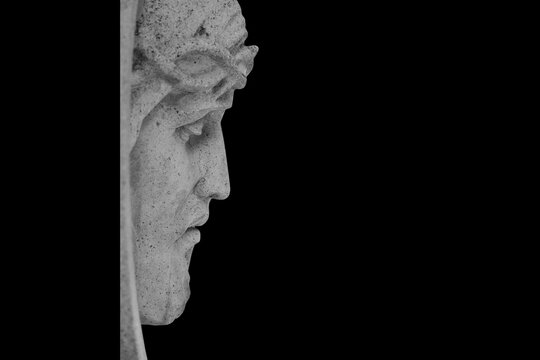Face of Jesus Christ in a crown of thorns against black background. Fragment of an ancient statue. Profile image.