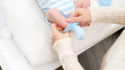 Closeup of mother dressing her little newborn baby son and putting on blue socks on tiny feet. Concept of babies and newborn hygiene and healthcare. Caring parents with little children.