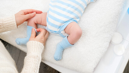 Closeup of young mother dressing her little baby son in socks while changing clothes on table....