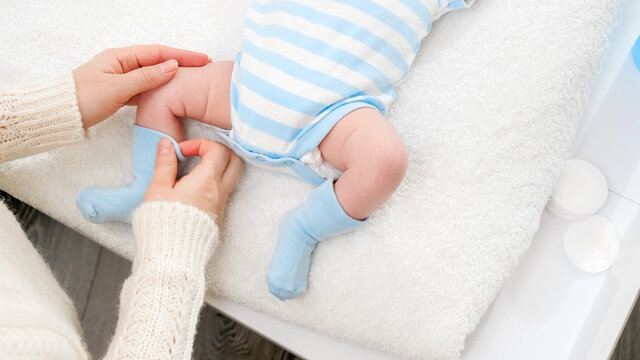 Closeup of young mother dressing her little baby son in socks while changing clothes on table. Concept of babies and newborn hygiene and healthcare. Caring parents with little children.