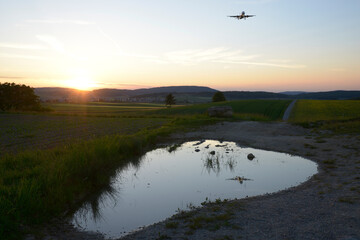 Obraz na płótnie Canvas avion en cours d'atterrissage en reflet dans l'eau au coucher du soleil