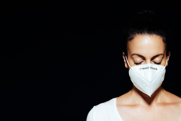 Woman with closed eyes wearing a FFP2 face mask against a dark background