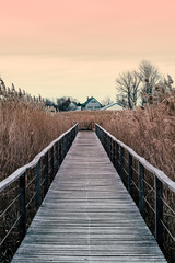 Wooden walkway bridge reaching into a lake. Cute house in the far. Orange and yellow sunset sky. Calm and relaxed mood