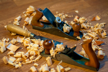 An old wooden jointer and a chisel with shavings lie on the wooden floor. Selective focus. 