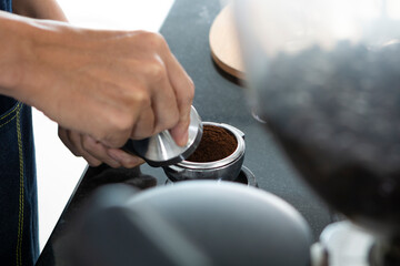 Closeup of Barista hand holding ground coffee for preparing espresso. Barista preparing portafilter before making cappuccino in a coffee shop. Barista preparing cup of coffee.