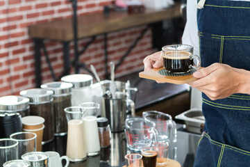 Hands of barista holding cup of hot coffee in the cafe shop. Barista holding a cup of coffee and smelling the black coffee, standing behind counter in modern coffee shop. 