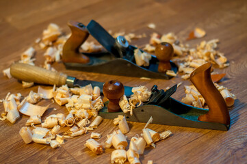 An old wooden jointer and a chisel with shavings lie on the wooden floor. Selective focus. 
