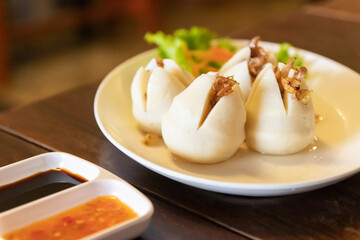 Boiled fish balls in white dish with sweet and spicy dipping sauce on wooden table.