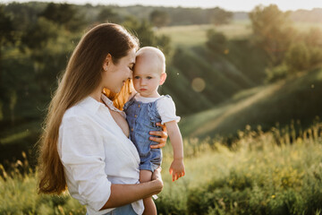 Fototapeta premium Young beautiful mother with her little daughter hug, kiss, laugh and walk in nature at sunset. Photo of a mother with a small child at sunset.