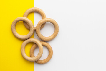 Five wooden rings on white-yellow background. Natural wood baby teether. Eco-friendly children toy. Top view, flat lay with copy space.