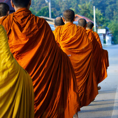 monks dressing orange robe during reception of alms, around buddhist temple