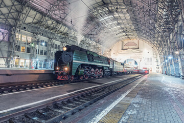 Retro steam train stands by the passenger platform.