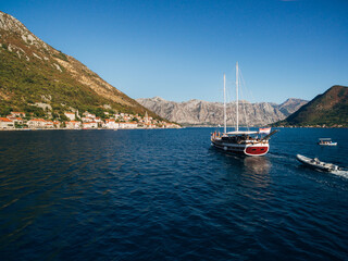 A large wooden sailing yacht sails against the backdrop of the city of Perast in Montenegro.