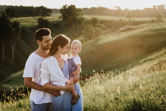 Young beautiful family with a little daughter hug, kiss and walk in nature at sunset. Photo of a family with a small child in nature.