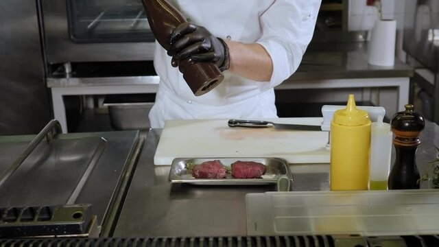 Close-up of the chef salting and peppering beef steak in the restaurant kitchen, the process of cooking delicious juicy meat.