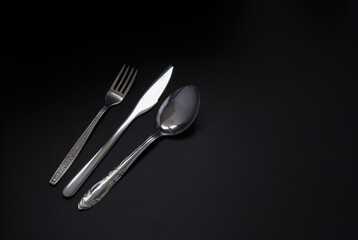 fork, spoon and knife on a dark background. Copy space