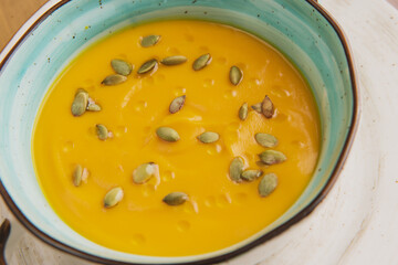 pumpkin soup with seeds in a beautiful plate on the background of the table and chopped pieces of pumpkin