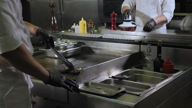 Close-up of the chef frying a juicy steak on the grill in the restaurant kitchen, the process of cooking meat on the grill with garlic and a sprig of rosemary.
