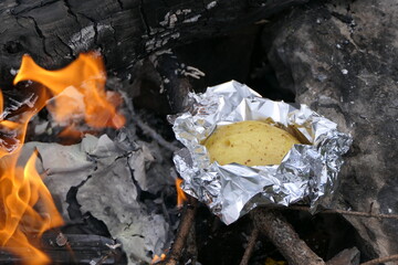 Barbecue and fireplace scene with roast potato in aluminum foil, embers, charred wood and fire flames